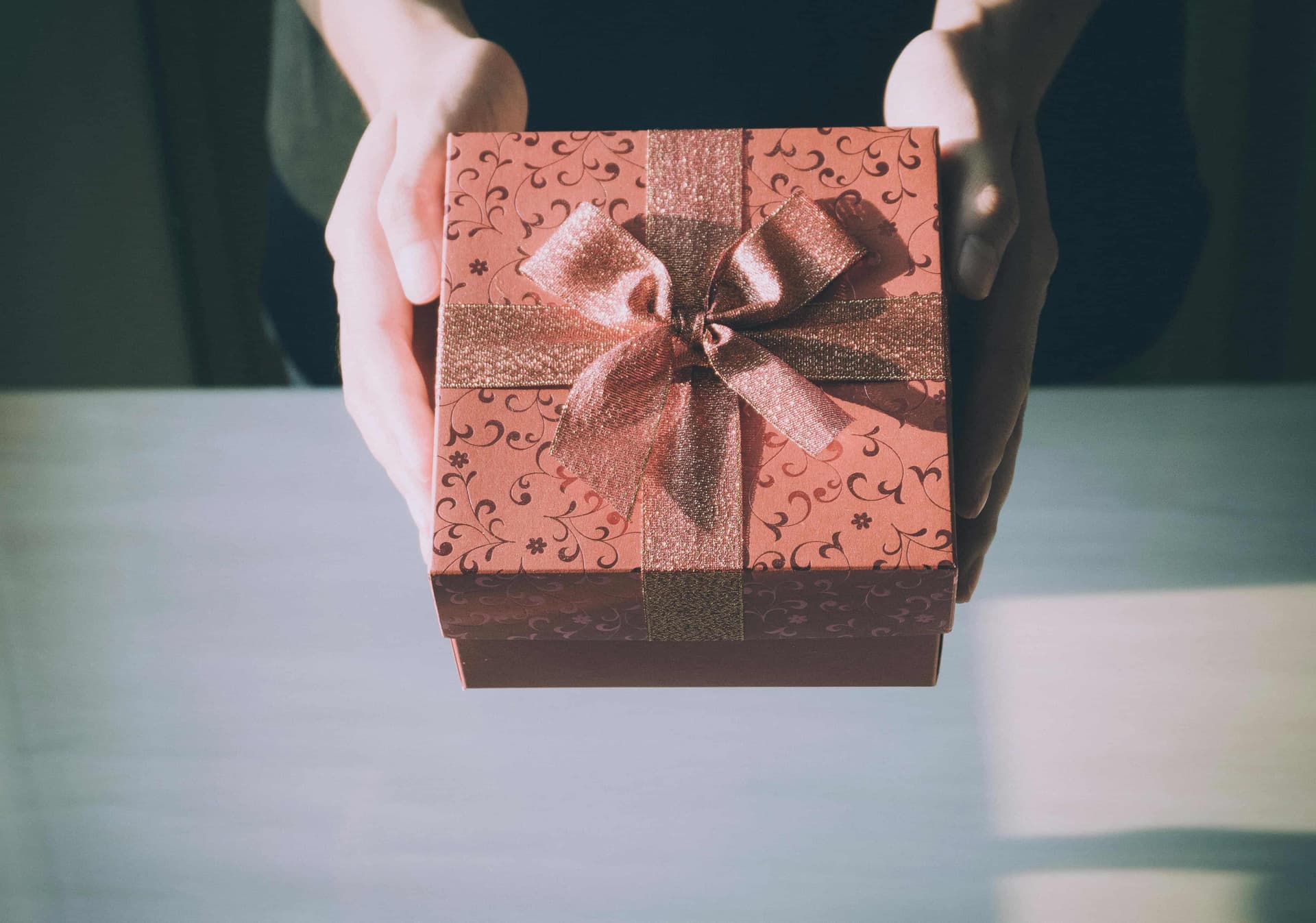 Mano entregando un regalo en una caja roja con estampado de flores